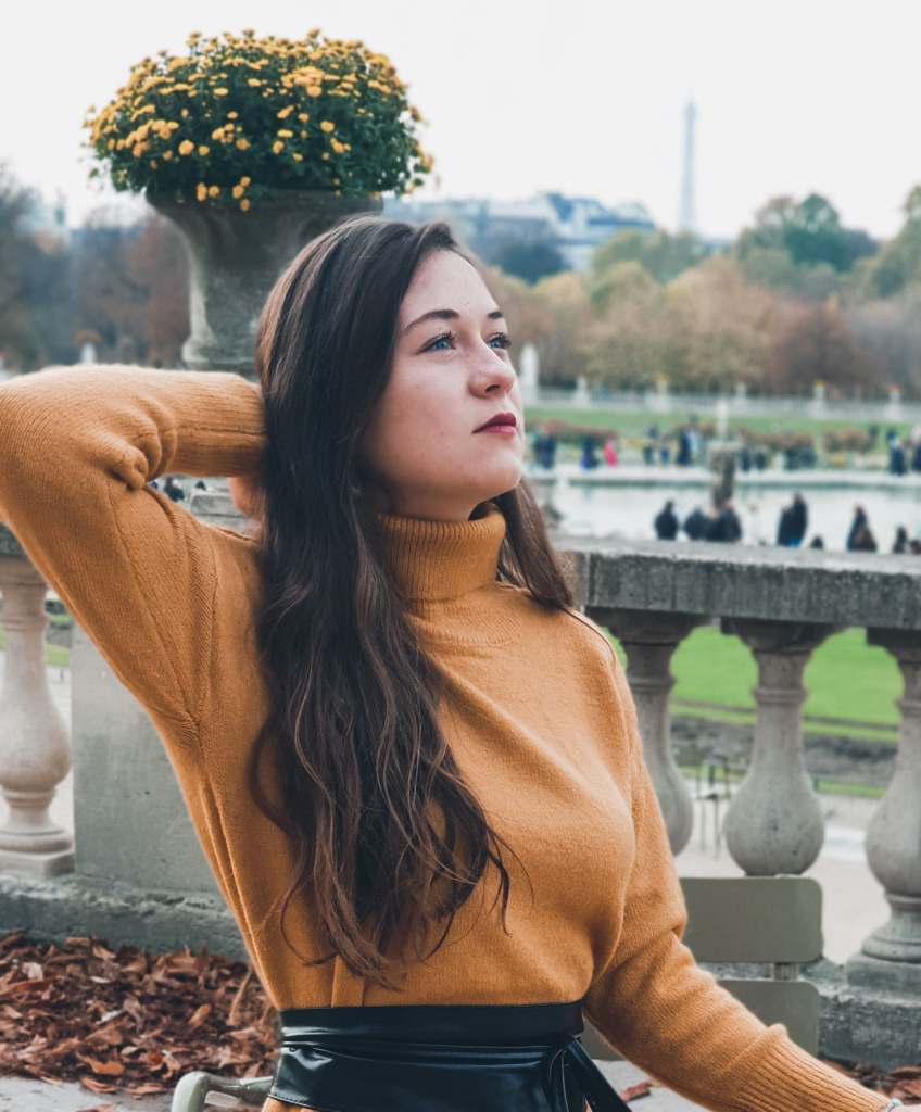 Jeune fille qui pose dans le Jardin du Luxembourg à Paris. Yeux bleux. Robe Pull jaune moutarde.